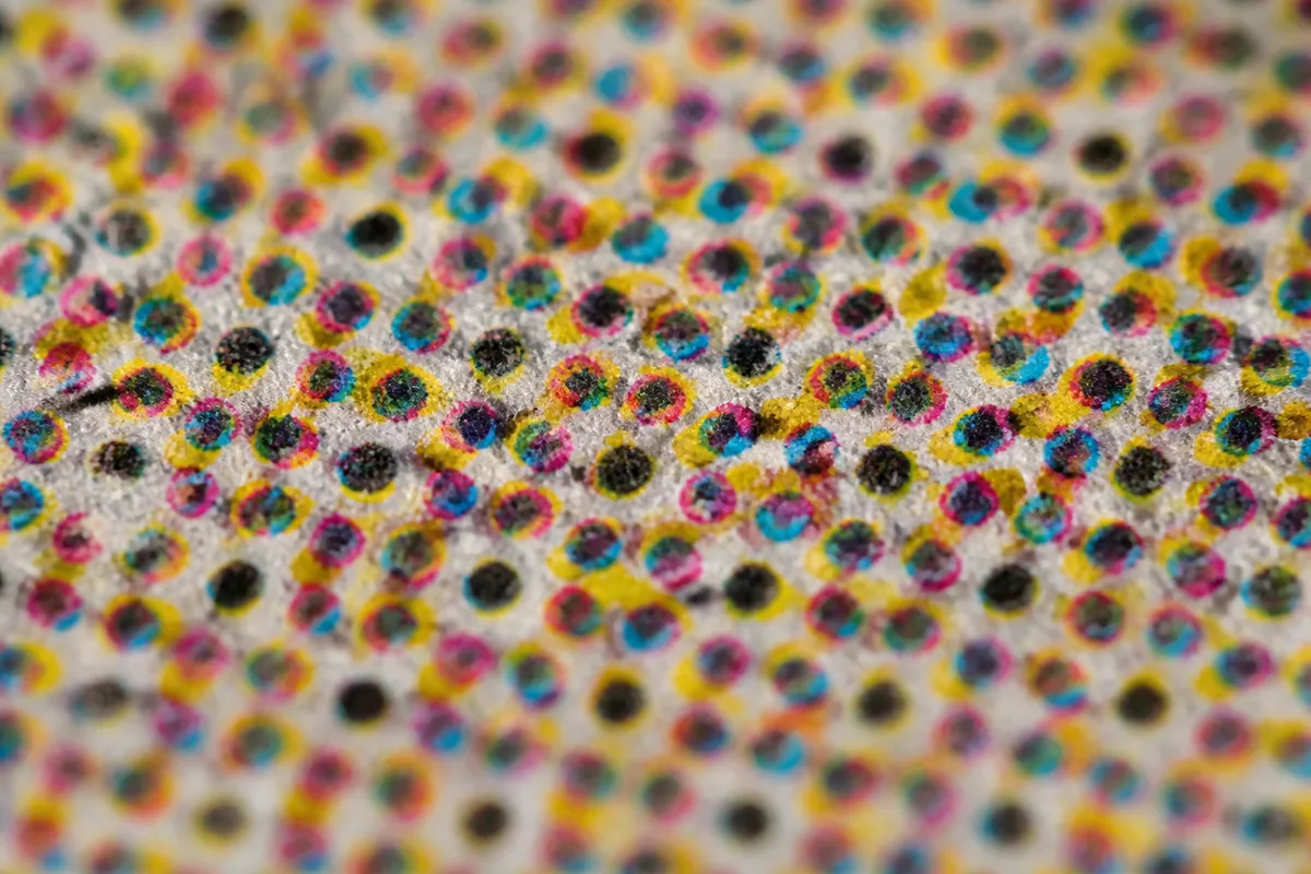 Détail macro d&rsquo;un imprimé montrant la rosette de points cyan, magenta, jaune et noir de la trame quadri